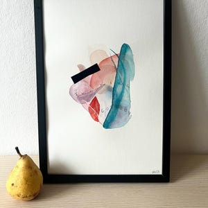 Könnte beinhalten: Abstrakter Aquarelldruck in einem schwarzen Rahmen. Das Kunstwerk zeigt eine Mischung aus rosa, roten und türkisfarbenen Aquarellformen, wobei die Worte "Fucking Gorgeous" teilweise sichtbar sind. Eine gelbe Birne befindet sich links von der gerahmten Kunst.