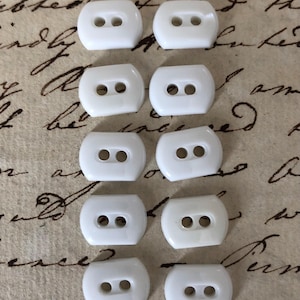 May include: Ten white plastic buttons with two holes each. The buttons are oval shaped and have a smooth, glossy finish.