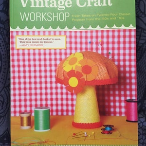 May include: A book cover for Vintage Craft Workshop, featuring a yellow and orange mushroom pincushion with red and white gingham fabric in the background. The book title is "Vintage Craft Workshop" and the subtitle is "Fresh Takes on Twenty-Four Classic Projects from the '60s and '70s".