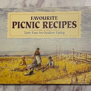 Może przedstawiać: Okładka książki z tytułem "FAVOURITE PICNIC RECIPES" i podtytułem "Tasty Fare for Outdoor Eating". Obraz przedstawia scenę piknikową na polu. Kolorystyka jest stonowana, z żółtymi, brązowymi i niebieskimi odcieniami.