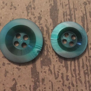 May include: Two green plastic buttons with four holes each. The buttons have a marbled pattern and a raised centre.