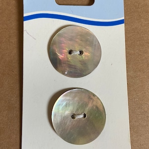 May include: Two white mother of pearl buttons with two holes each, packaged on a white card with the word "COATS" printed in blue.