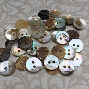 May include: A collection of round buttons in various colors and textures. The buttons have two or four holes for sewing. Colors include cream, brown, black, and iridescent pearl. The buttons are made of natural materials.