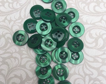 May include: A pile of 18 green plastic buttons with five holes each. The buttons are shiny and have a slight sheen.
