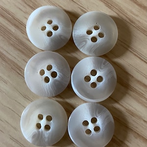 May include: Six white buttons with a swirl pattern and four holes each.