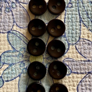 May include: Ten black plastic buttons with two holes each. The buttons are arranged in two rows of five.