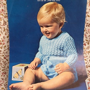 May include: A knitting pattern booklet featuring a baby wearing a blue knitted onesie. The booklet is titled "Brilliante Quickerknit" and has the number 6271 on the cover. The pattern is for a 18-19 inch (46-48 cm) garment.