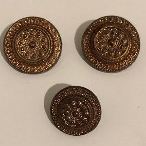 May include: Three gold-coloured metal buttons with intricate circular designs. The buttons have a raised centre with a smaller circle in the middle.