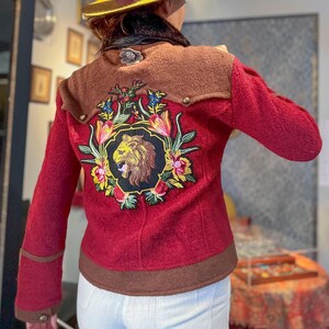 May include: A red wool jacket with a brown collar and brown trim. The jacket has an embroidered lion design on the back with colorful flowers and leaves.