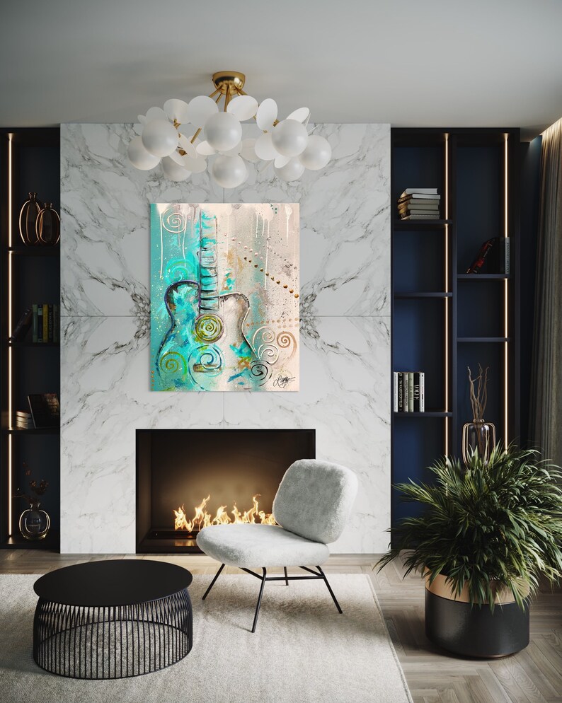 May include: A teal and white abstract painting of a guitar with gold accents hanging on a white marble wall above a fireplace. The fireplace has a black surround and a fire burning inside. A white chair sits in front of the fireplace.