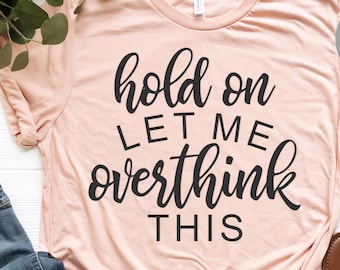 May include: A light pink t-shirt with black text that reads "hold on let me overthink this".
