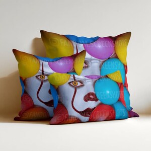 May include: Two decorative throw pillows featuring a clown face design with red, white, and blue accents. The pillows are adorned with colorful balloons in yellow, purple, and blue. The design is printed on a white background.