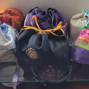 May include: A collection of ten drawstring bags in various colors and patterns, including red, blue, yellow, green, and black. The bags are made of fabric and have a variety of designs, including floral, geometric, and paisley.