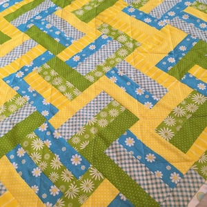 May include: A quilt with a patchwork design featuring yellow, green, and blue fabric. The fabric has a floral pattern with white daisies.