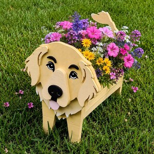 May include: A light yellow wooden planter shaped like a golden retriever dog, featuring a painted face with black eyes, a black nose, and a pink tongue. The planter is filled with a vibrant arrangement of pink, yellow, purple, and white flowers.