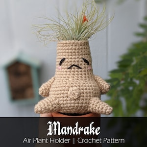 Puede incluir: Un soporte para plantas aéreas de mandrágora tejido a crochet con una cara triste. El soporte es beige y tiene una pequeña planta aérea que crece en la parte superior. El texto "Mandrake" está escrito en una fuente gótica debajo del soporte. El texto "Soporte para plantas aéreas | Patrón de crochet" está escrito debajo de la palabra "Mandrake".