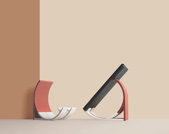 May include: Two red and white modern minimalist phone stands with a black phone resting on one of the stands.