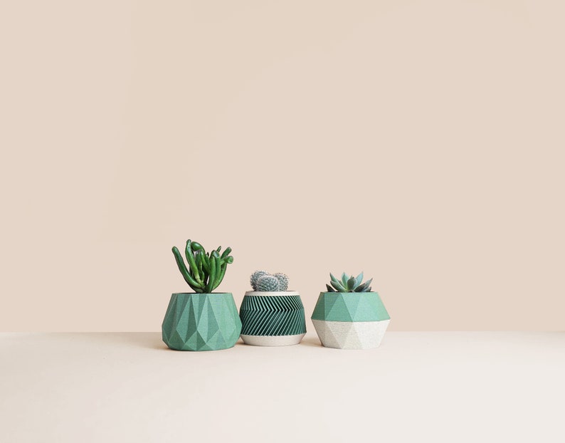 May include: Three geometric succulent planters in green and white. The planters are made of a textured material and have a modern design.
