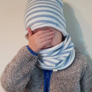 Puede incluir: Un ni&ntilde;o con una chaqueta gris peluda con una cremallera azul y un gorro y un cuello de cuello azul y blanco a rayas.
