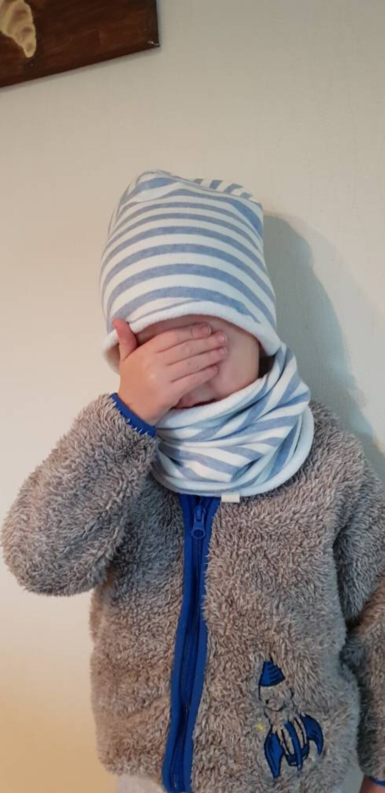 Puede incluir: Un ni&ntilde;o con una chaqueta gris peluda con una cremallera azul y un gorro y un cuello de cuello azul y blanco a rayas.