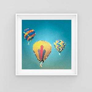 May include: Three hot air balloons in the sky. The largest balloon is yellow with red and black accents. The other two balloons are smaller and have a multi-colored pattern.
