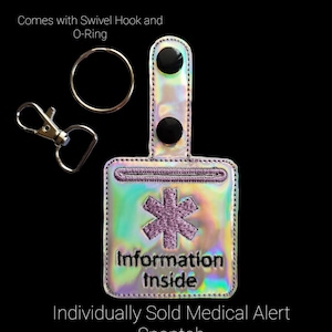 May include: Iridescent medical alert snaptab with a purple star of life symbol and the words "Information Inside." Includes a swivel hook and O-ring. The text "Individually Sold Medical Alert Snaptab" is also visible.