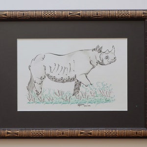 Peut inclure: Un dessin au trait noir et blanc d'un rhinocéros debout dans un champ d'herbe. Le dessin est encadré dans un cadre brun foncé avec une bordure dorée à motifs.
