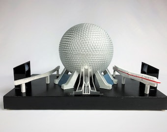Könnte beinhalten: Ein Modell der Spaceship Earth Attraktion im Epcot, mit einer silbernen geodätischen Kugel auf einem schwarzen Sockel und einer Monorail-Strecke.