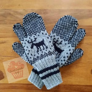May include: A pair of knit mittens featuring a dark navy blue and light grey colour scheme. The mittens display a repeating geometric pattern and a central silhouette of a reindeer. The cuffs are ribbed with two horizontal navy blue stripes.