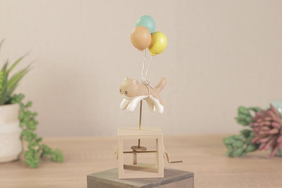 A whimsical handmade automaton of a cat floating away under a balloon — charming, original concept that cat people will immediately want.