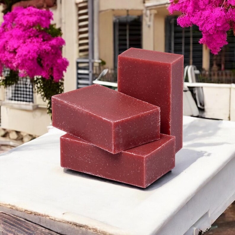 May include: Three bars of deep red soap stacked on top of each other. The soap has a speckled appearance.