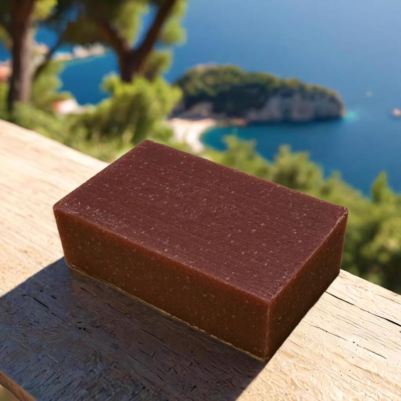 May include: A rectangular bar of dark brown soap with a grainy texture. The soap is sitting on a wooden surface.