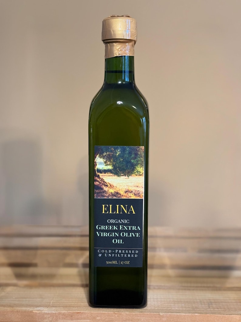 May include: A green glass bottle of Elina Organic Greek Extra Virgin Olive Oil. The label features a landscape image and text. The bottle is 17 oz and has a gold foil seal on the top.