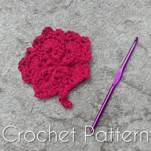 May include: A close-up of a bright pink crochet flower with a purple crochet hook. The text "Crochet Pattern" is visible at the bottom of the image.