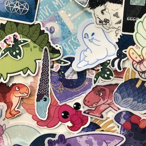 May include: A collection of colourful stickers featuring various designs, including a dinosaur, a ghost, a crab, a sea creature, and a dinosaur. The stickers are on a white background with a glittery texture.