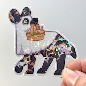 May include: A holographic sticker of a cartoon African wild dog wearing a ghost costume and carrying a basket of fruit. The dog has black, brown, and white spots.