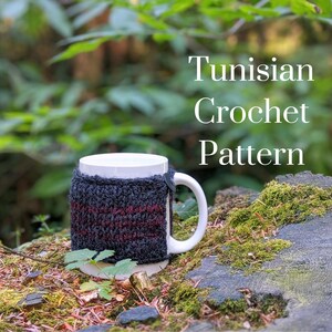May include: A white ceramic mug with a black and burgundy crocheted cozy. The cozy has a button closure. The mug is sitting on a mossy rock with the text "Tunisian Crochet Pattern" in white text above it.