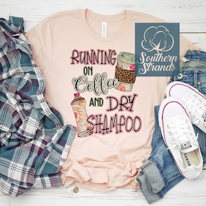 May include: A pink t-shirt with the text "Running on Coffee and Dry Shampoo" in black and pink lettering. The shirt also features a graphic of a coffee cup and a bottle of dry shampoo.