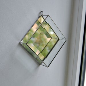 Könnte beinhalten: Ein quadratisches, verspiegeltes Glasobjekt mit einem Metallrahmen. Der Spiegel besteht aus kleineren, abgewinkelten Glasscheiben, die einen Kaleidoskopeffekt erzeugen.