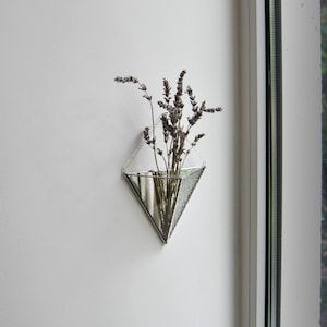 May include: A silver mirrored triangle vase with dried lavender flowers hanging on a white wall.