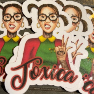 May include: A sticker featuring a cartoon illustration of a girl with pigtails wearing glasses and a red and green outfit. The girl has tattoos and is making a peace sign with her hands. The sticker has the word "Toxica" written in black cursive lettering.