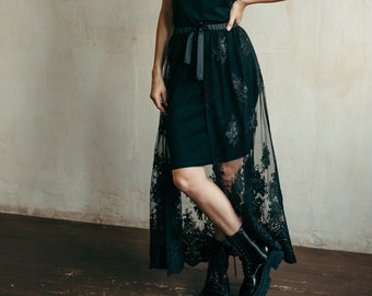 May include: A woman wearing a black dress with a lace overlay and black lace-up boots. The dress has a black ribbon tied at the waist.