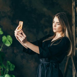 Bridesmaid is taking a selfie while wearing a handmade black bridal robe.
