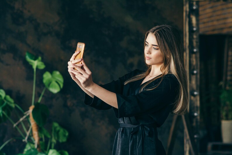 Bridesmaid is taking a selfie while wearing a handmade black bridal robe.