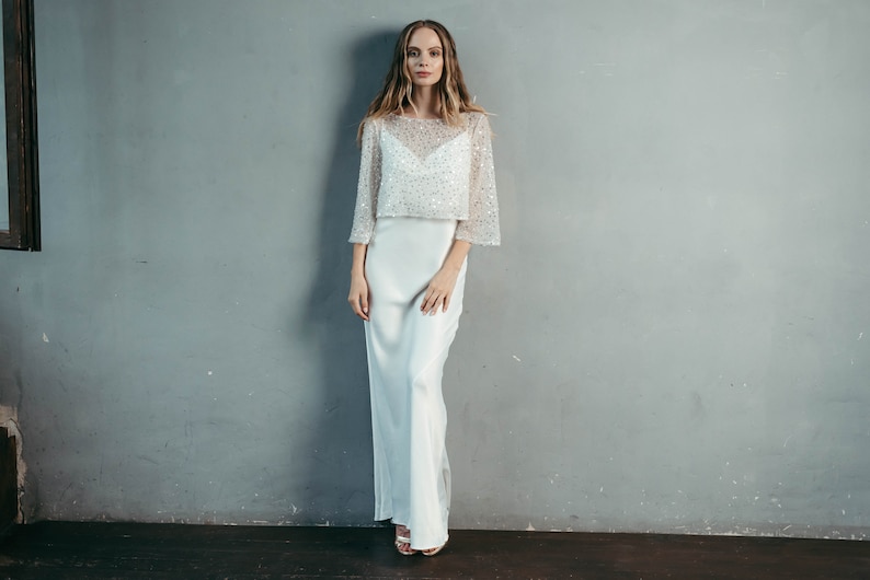 May include: A white, long-sleeved, beaded top with a matching white satin skirt. The top has a scoop neckline and a loose, flowing fit. The skirt is fitted at the waist and flows to the floor.