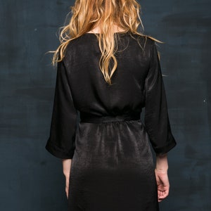 A black satin robe with long sleeves and a tie belt. The dressing gown is knee-length and has a simple, elegant design.