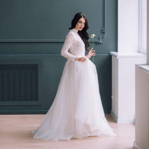 Bride wearing ivory lace top with full tulle skirt, holding bouquet indoors.