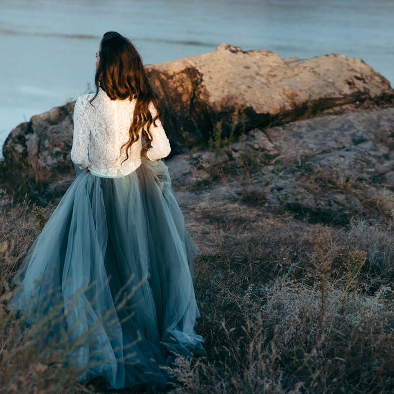 Bride in ivory lace high neck top with teal tulle skirt, photographed outdoors by the sea.