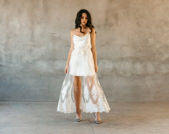 May include: A white satin dress with a cowl neck and a lace overlay. The dress has a fitted bodice and a flowing skirt.