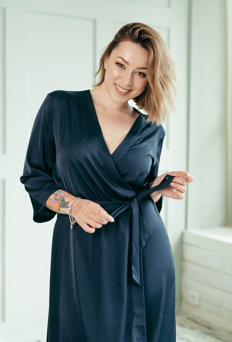 May include: A woman wearing a dark blue satin robe with a wrap style and a tie at the waist.